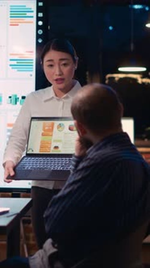 Vertical Video Asian Employee Presenting Revenue Report Showing Charts on Laptop