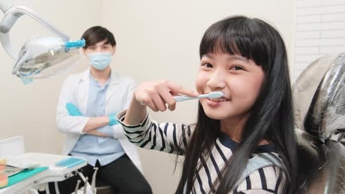 Portrait of an Asian girl with a male pediatric dentist in dental clinic.