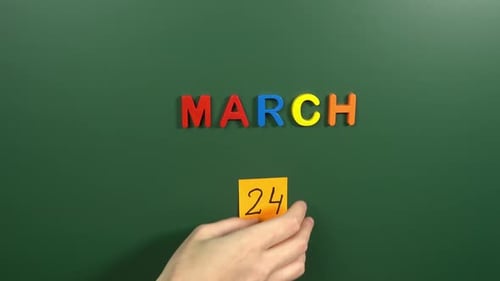 Hand sticking a sticker 24 March calendar day on school board. 24 date of March. Twenty fourth day