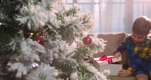 Excited Child Opens Christmas Gift by Decorated Tree