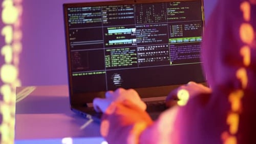 Un hacker vêtu d'un sweat-shirt à capuche écrit du code sur un terminal portable contenant des journaux système, des données réseau et