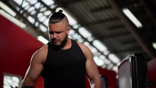 Bearded Man in Black Tank Top Performing Bicep Curl with Dumbbell in Gym Demonstrating Strength and