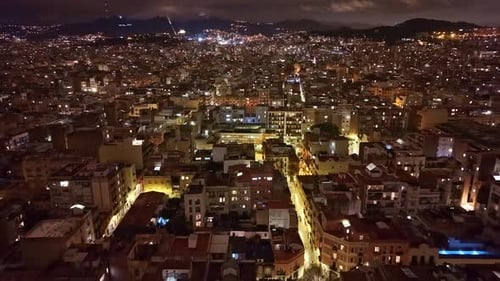 Wide nighttime aerial of Barcelona showing dense urban blocks, glowing arterial streets, and