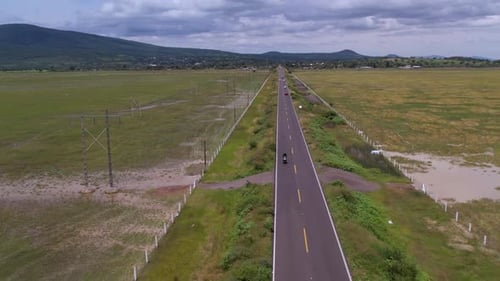 aerial shot of a motorcycle on a road and a green meadow on both sides