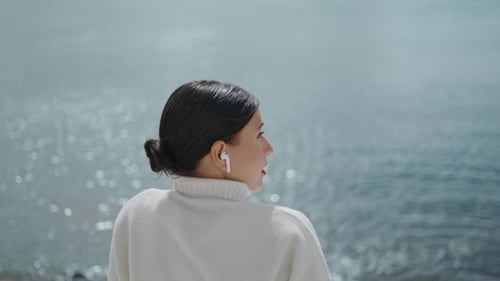 Relaxed Girl Listening Music in Wireless Earbuds Sitting at Waterfront Close Up