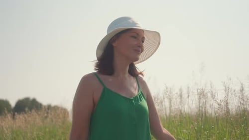 Young Woman Walking Through Barley Field in Sunhat and Green Dress