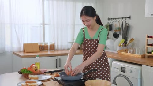 Woman Cracking Egg into Pan in Bright Kitchen