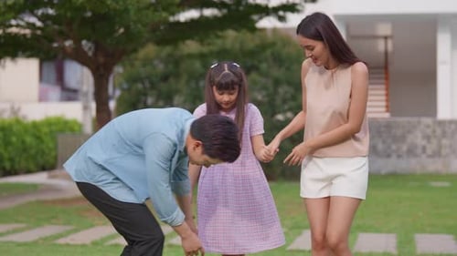 Asiatisch liebende Eltern spielen mit ihrer kleinen Tochter draußen im Garten.
