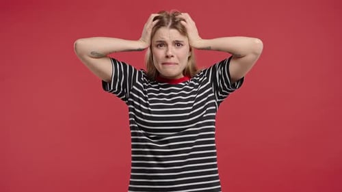 Distressed woman with hands on head against red background