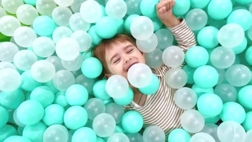 A Little Boy is Playing in a Children's Center on a Slide and Falls Into a Pool with Colored Balls