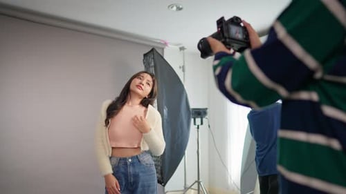 Asian woman model being photographed by cameraman in a photography studio.