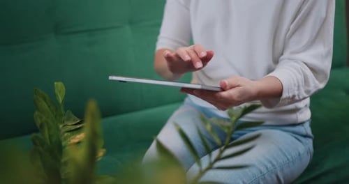 Woman touching screen of digital tablet, hands of close-up. Businesswoman sitting on couch distance