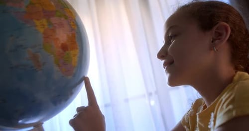 Girl Examines Globe Near Sunny Window