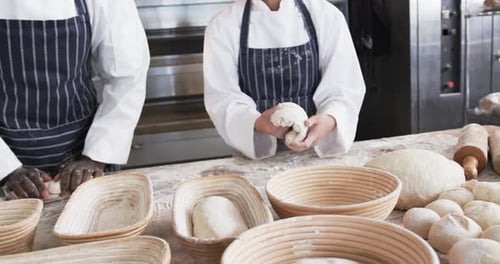 Midsection of diverse bakers working in bakery kitchen, forming bread form dough, slow motion