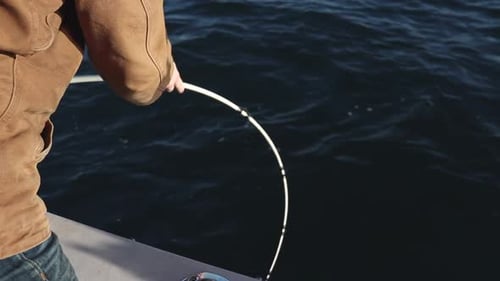 Mann, der große Fische an einer Angelrute anzieht. Angelrute, die sich beim Angeln auf dem Boot im Wasser biegt. Catchi