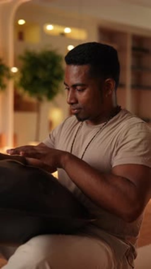 Vertical Shot of Happy African Young Man in Trance Sitting Playing on Steel Tongue Drum on Floor at