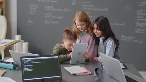 Drei fröhliche Grundschüler schauen auf Tablet