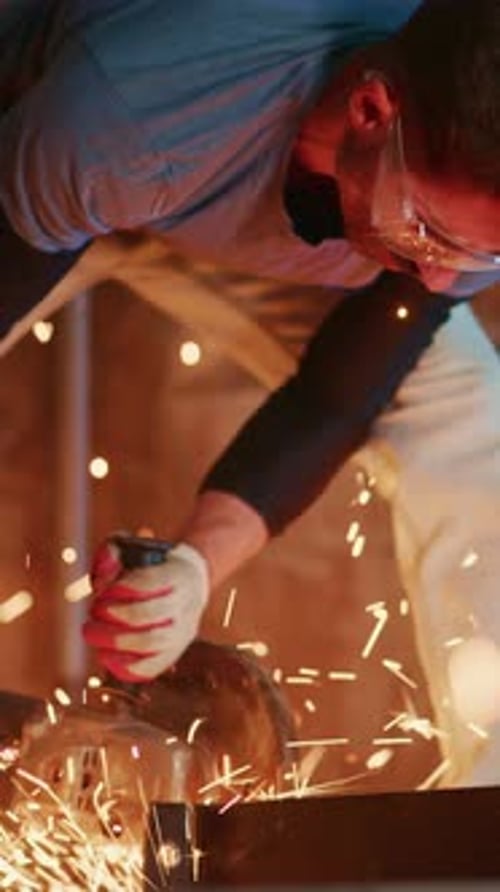 Man Using Angle Grinder in a Dark Workshop