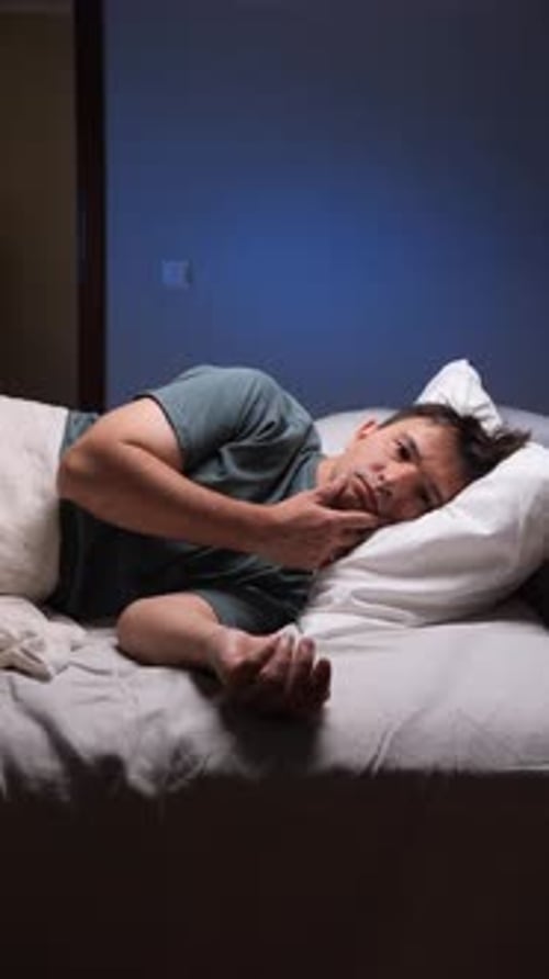 Vertikales Video Schlafloser Mann, der nachts im Bett liegt und an Schlaflosigkeit leidet