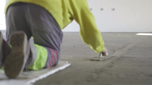 Static view of a labourer levelling the plastered floor using flat trowel and cement manually wearin
