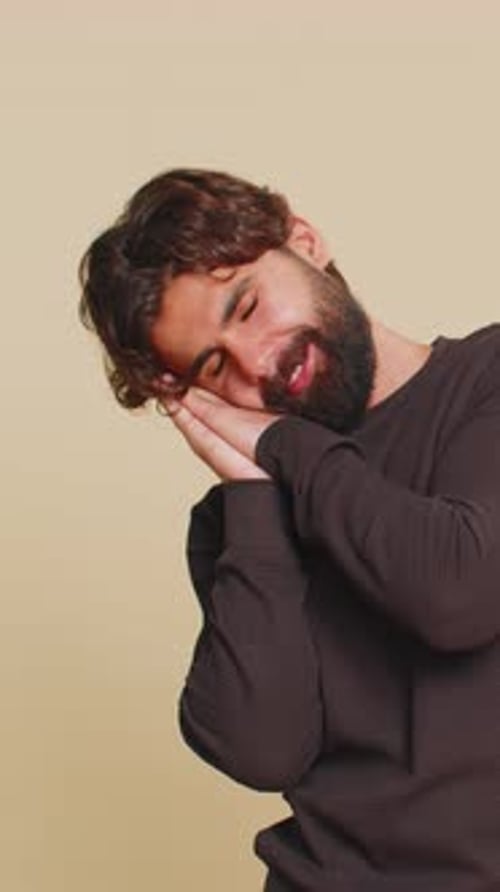 Man Mimes Sleeping Against Beige Backdrop