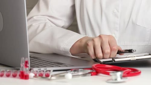 Medical Professional Writing Notes Then Typing on Laptop