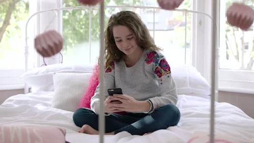 Teenage Girl Using Mobile Phone on Bed Indoors
