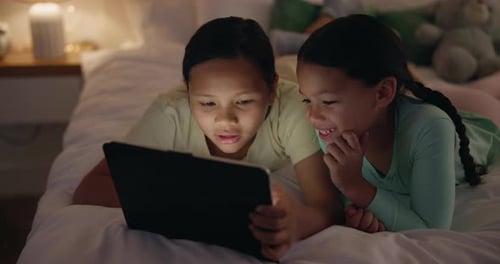 Girls Using Tablet Together on Bed at Night