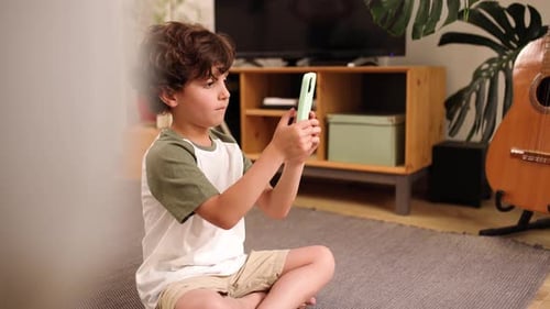 Boy Sitting Cross Legged Taking Pictures with Phone