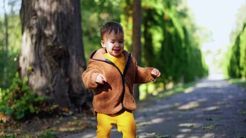 Energetic cheerful Caucasian toddler jumping happily outdoors. Cute baby boy walking in the park.