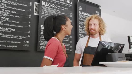 Happy diverse male and female baristas wearing aprons talking behind the coiunter in cafe
