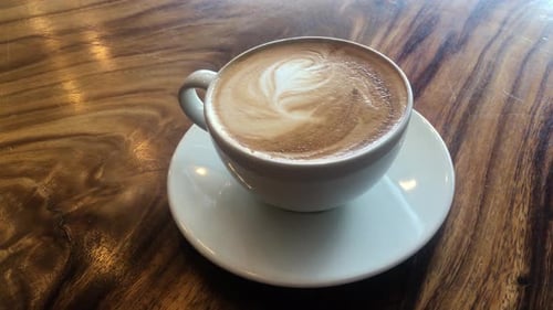 Latte art in white cup on wooden background, slow zoom
