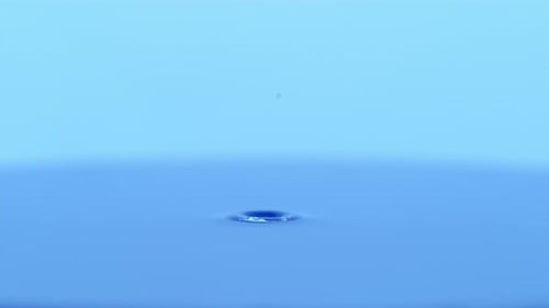 Water Drop Impacting Blue Liquid Surface With Ripples