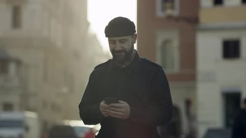 Smiling Italian Man Looking Down And Using His Mobile Phone In The Middle Of A Street In Rome, Wi...