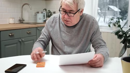 Senior Adult Calculates Bills at Kitchen Table