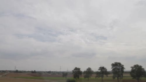 Landschaft, die von einem fahrenden Zug aus gesehen wird und Felder und einen bewölkten Himmel einfängt