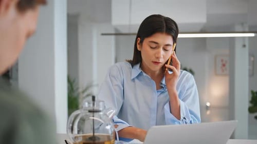Woman Using Laptop and Talking on Smartphone in Office