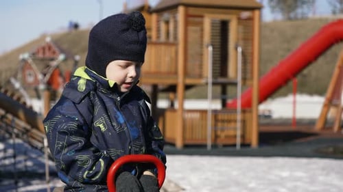 Child playing on a seesaw in winter clothes at the playground