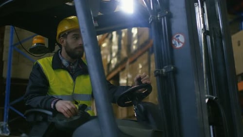 Close-up Shot of a Forklift Driver Operating Vehicle in a Big Warehouse full of Pallet Rack.
