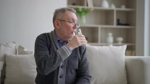 Durstiger älterer Mann trinkt klares Wasser Älterer grauhaariger Mann mit Brille kümmert sich um die Gesundheit
