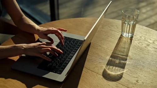 Ansicht von oben auf eine nicht wiederzuerkennende Geschäftsfrau, die auf der Laptoptastatur tippt, während sie von zu Hause aus arbeitet