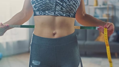 Close Up of a Strong and Beautiful Busty Fit Girl in an Athletic Top Measuring Her Waist With a Tap