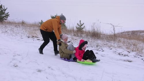 A Snow Slide Where a Family is Having Fun on Plastic Sleds Winter Fun