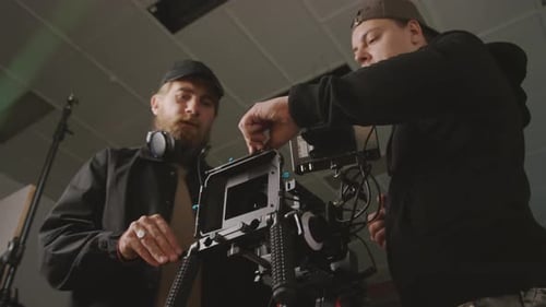 Two Cameramen Setting up Equipment for Filming in Studio