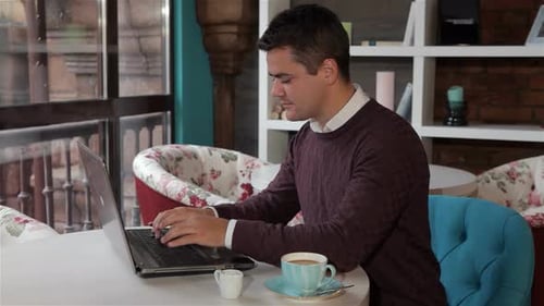Focused Man Working on Laptop in a Cozy Cafe