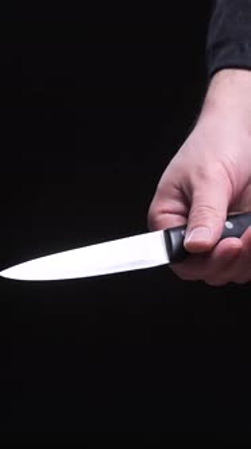 Vertical Video Criminal Hand Holding Knife in Threatening Posture on Dark Background