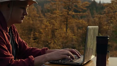 No verão, uma pessoa viaja com responsabilidade. O viajante está trabalhando em um laptop. Nas montanhas