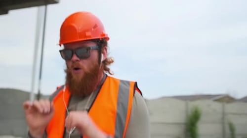 Cool construction worker at construction site dancing end of work shift in uniform and safety helmet