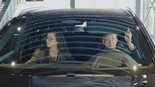 Young Couple Sitting in New Car in Showroom and Discussing Its Features