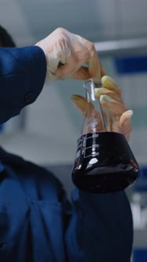 Des femmes scientifiques vêtues de blouses de laboratoire protectrices examinent une solution chimique violet foncé dans un erlenmeyer